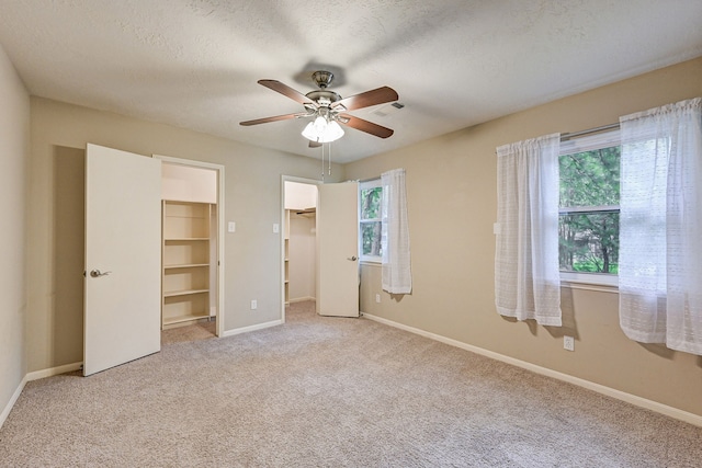 unfurnished bedroom with ceiling fan, multiple windows, a walk in closet, and light colored carpet