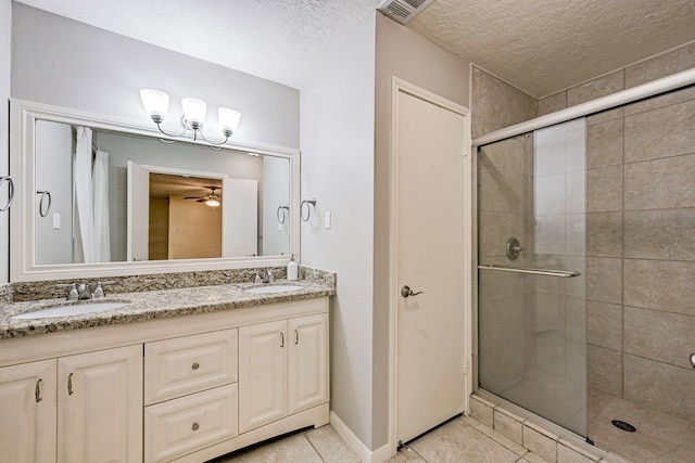 bathroom with a shower with shower door, a textured ceiling, tile patterned flooring, dual bowl vanity, and ceiling fan