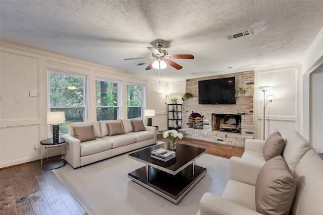 living room featuring ceiling fan, a textured ceiling, a fireplace, and wood-type flooring