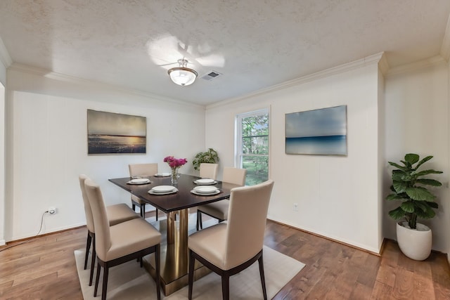 dining space with a textured ceiling, crown molding, and hardwood / wood-style flooring