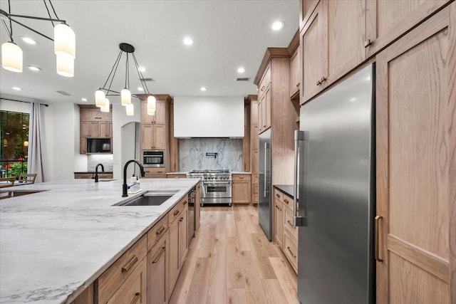 kitchen featuring sink, decorative backsplash, hanging light fixtures, high end appliances, and light wood-type flooring