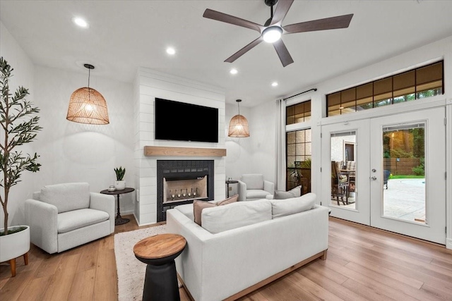 living room with a fireplace, french doors, ceiling fan, and light wood-type flooring