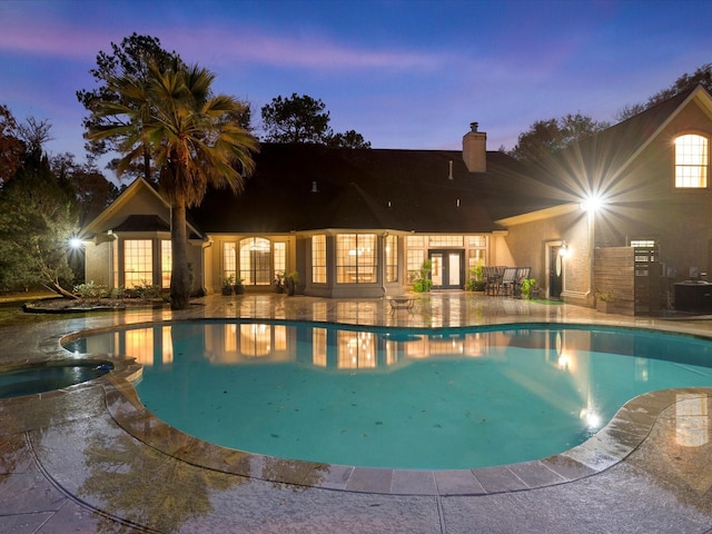 pool at dusk featuring cooling unit, a patio, french doors, and an in ground hot tub