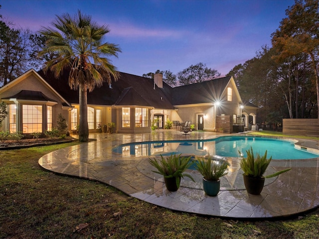 pool at dusk featuring a diving board and a patio