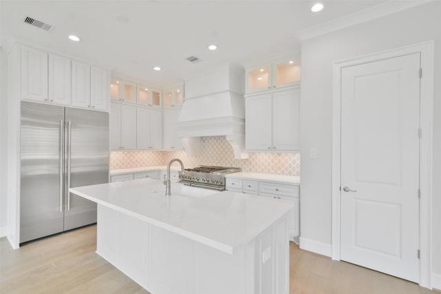 kitchen featuring tasteful backsplash, a center island with sink, white cabinetry, custom exhaust hood, and high end appliances