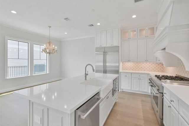 kitchen with an island with sink, high quality appliances, white cabinets, light hardwood / wood-style flooring, and decorative backsplash