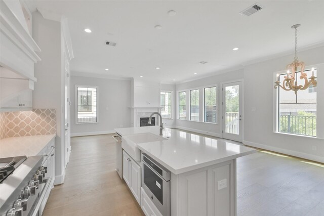 kitchen featuring appliances with stainless steel finishes, white cabinets, a center island with sink, and a healthy amount of sunlight