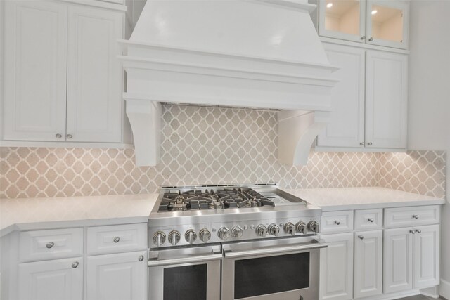 kitchen featuring tasteful backsplash, double oven range, custom range hood, and white cabinetry