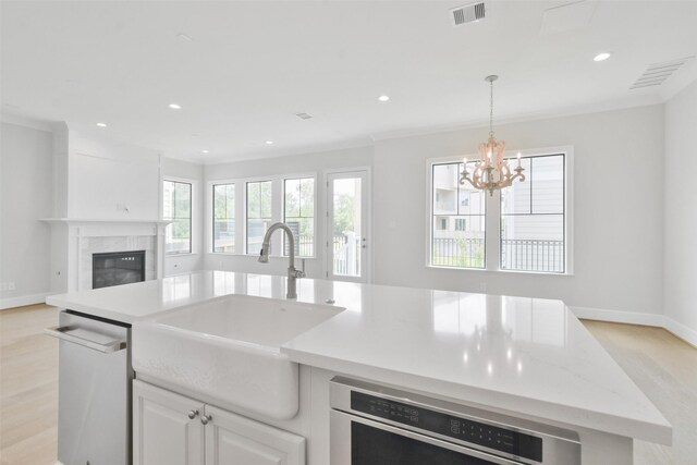 kitchen featuring a high end fireplace, light wood-type flooring, pendant lighting, dishwasher, and sink