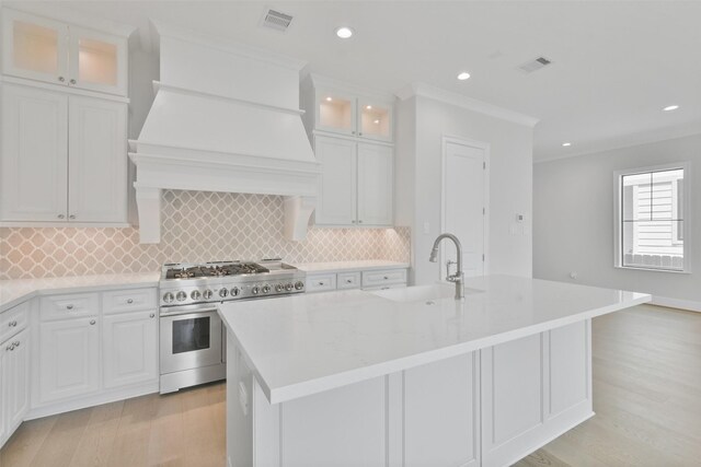 kitchen with an island with sink, tasteful backsplash, double oven range, and white cabinetry