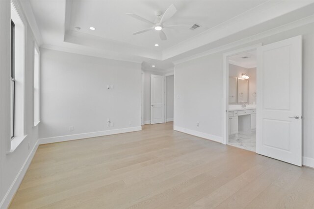 unfurnished bedroom featuring light hardwood / wood-style floors, ensuite bathroom, ceiling fan, and a raised ceiling