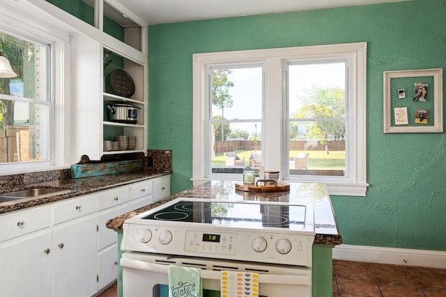 kitchen with white cabinets, plenty of natural light, dark stone counters, and electric range