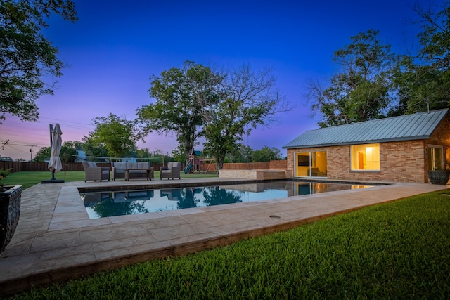 pool at dusk with a playground, outdoor lounge area, an outbuilding, a yard, and a patio area