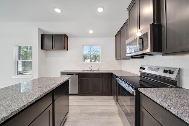 kitchen featuring light stone countertops, sink, stainless steel appliances, backsplash, and light wood-type flooring