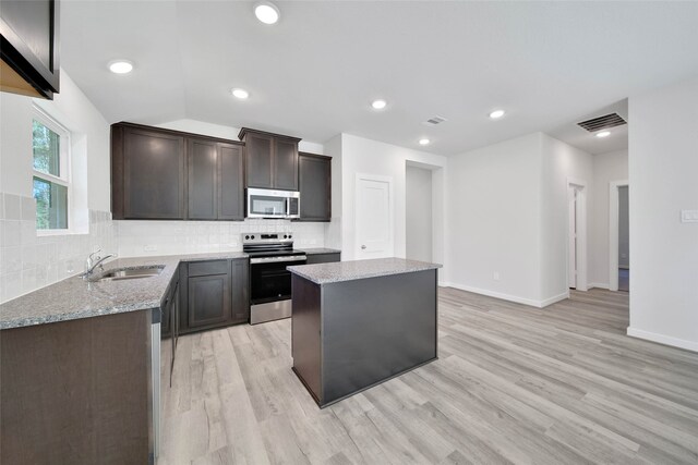 kitchen with sink, light stone counters, light hardwood / wood-style flooring, a kitchen island, and stainless steel appliances