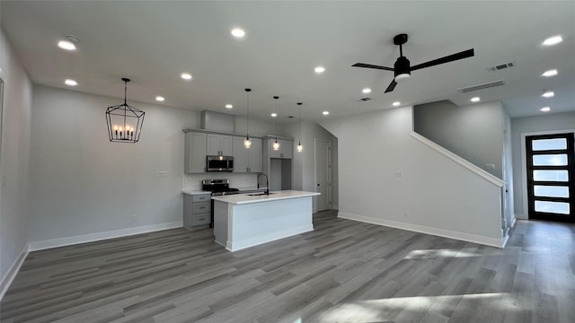 kitchen with appliances with stainless steel finishes, decorative light fixtures, a kitchen island with sink, and sink