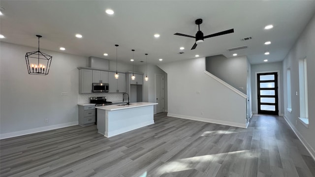 kitchen featuring appliances with stainless steel finishes, a center island with sink, hanging light fixtures, and gray cabinetry