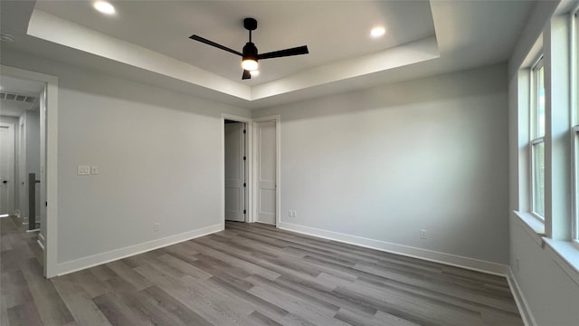 spare room featuring light wood-type flooring, a tray ceiling, and ceiling fan