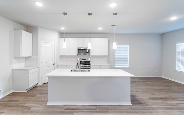 kitchen featuring white cabinets, an island with sink, sink, decorative light fixtures, and stainless steel appliances