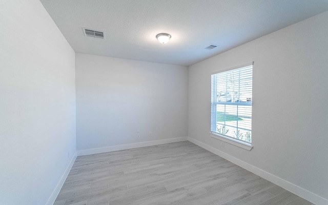 empty room featuring light wood-style floors, visible vents, and baseboards