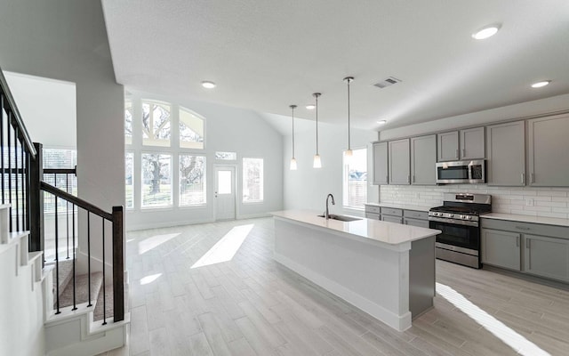 kitchen with lofted ceiling, visible vents, gray cabinetry, appliances with stainless steel finishes, and a sink