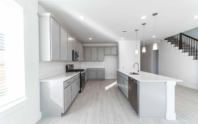 kitchen with decorative backsplash, decorative light fixtures, gray cabinets, stainless steel appliances, and a sink