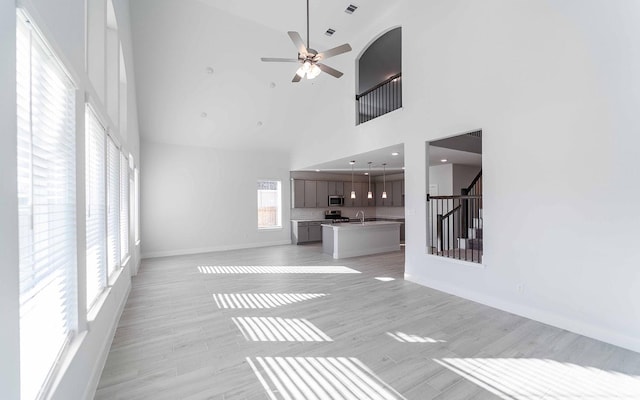 unfurnished living room featuring stairway, light wood-style floors, a ceiling fan, a sink, and baseboards