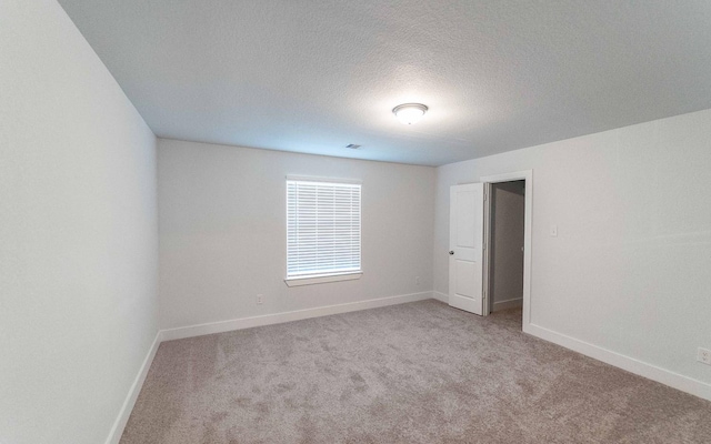 spare room featuring light colored carpet, a textured ceiling, and baseboards