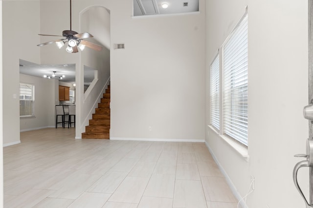 unfurnished living room with stairway, ceiling fan, a towering ceiling, baseboards, and visible vents