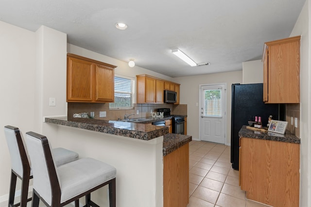 kitchen with a kitchen breakfast bar, a sink, black appliances, a peninsula, and tasteful backsplash
