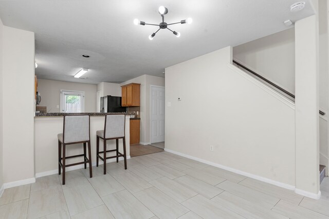 kitchen featuring black fridge, dark stone countertops, kitchen peninsula, a breakfast bar area, and a chandelier