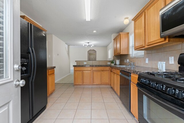 kitchen with sink, tasteful backsplash, light tile patterned floors, kitchen peninsula, and black appliances