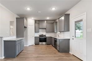 kitchen with backsplash, light hardwood / wood-style floors, stove, and gray cabinetry