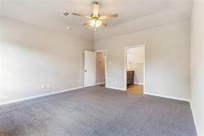 unfurnished bedroom with ensuite bathroom, dark colored carpet, and ceiling fan