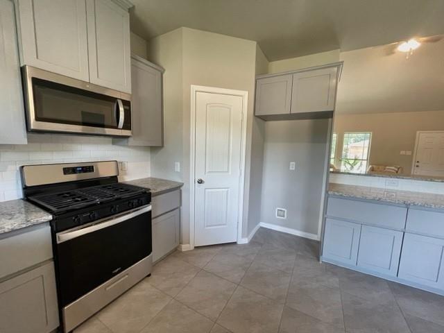 kitchen with backsplash, light stone countertops, light tile patterned floors, and stainless steel appliances