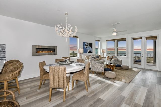 dining space with a water view, french doors, light wood-type flooring, and ceiling fan with notable chandelier