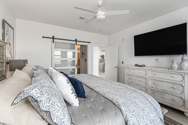 bedroom with a barn door, wood-type flooring, and ceiling fan