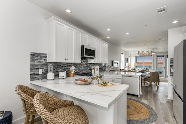 kitchen featuring appliances with stainless steel finishes, kitchen peninsula, white cabinetry, and a kitchen bar