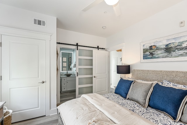 bedroom with ceiling fan, ensuite bath, light hardwood / wood-style flooring, and a barn door