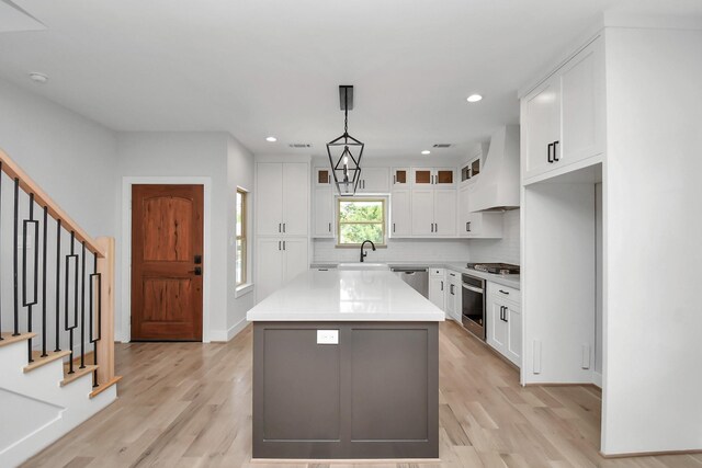 kitchen with white cabinets, light hardwood / wood-style floors, custom exhaust hood, and hanging light fixtures