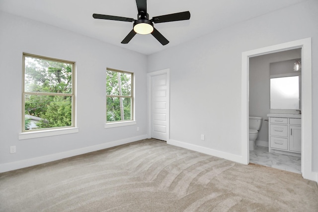 unfurnished bedroom featuring ensuite bath, light colored carpet, and ceiling fan