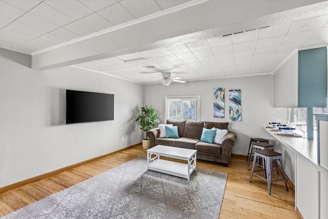 living area with ornamental molding, ceiling fan, light wood-style flooring, and baseboards