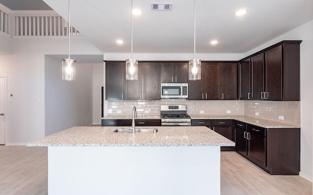 kitchen featuring dark brown cabinetry, sink, decorative light fixtures, stainless steel appliances, and a kitchen island with sink