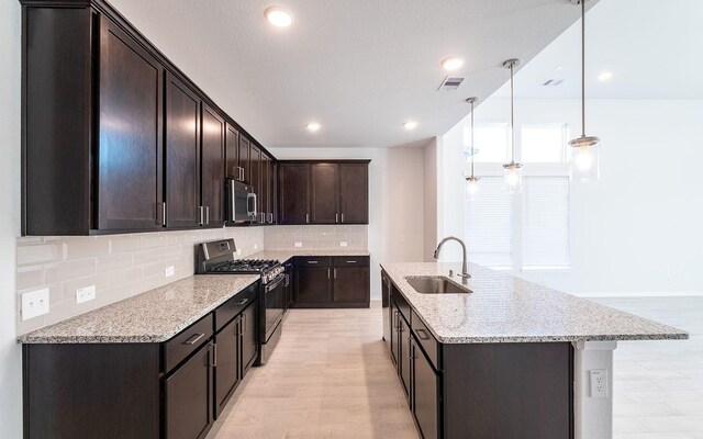 kitchen with light wood-type flooring, gas range, decorative backsplash, pendant lighting, and sink