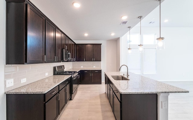 kitchen featuring sink, hanging light fixtures, light stone counters, stainless steel appliances, and dark brown cabinets