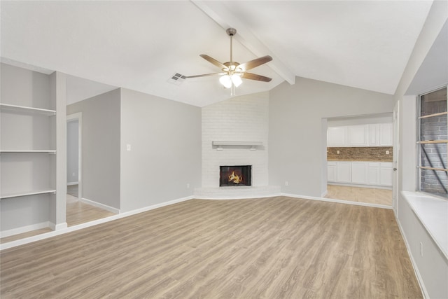 unfurnished living room with ceiling fan, brick wall, lofted ceiling with beams, light hardwood / wood-style flooring, and a brick fireplace