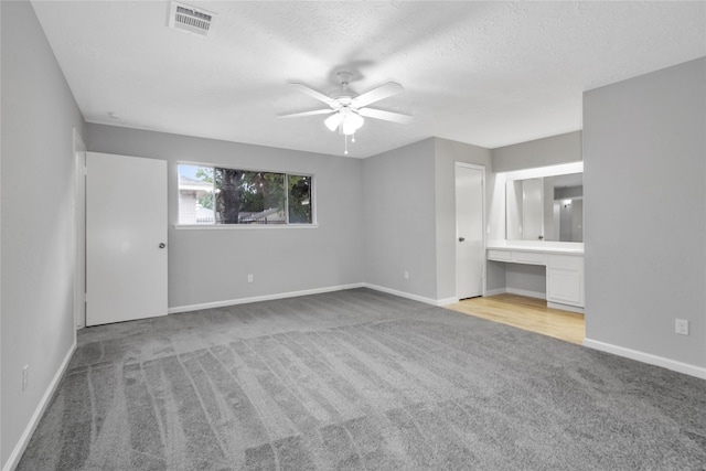 unfurnished bedroom featuring light carpet, ensuite bathroom, a textured ceiling, and ceiling fan