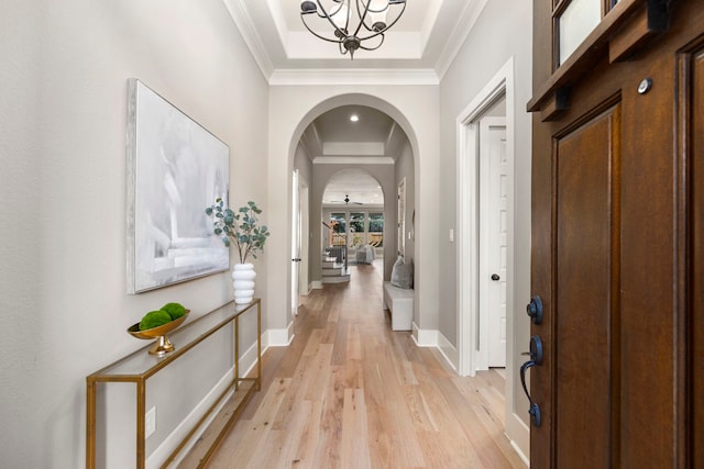 hall with a notable chandelier, crown molding, a raised ceiling, and light wood-type flooring