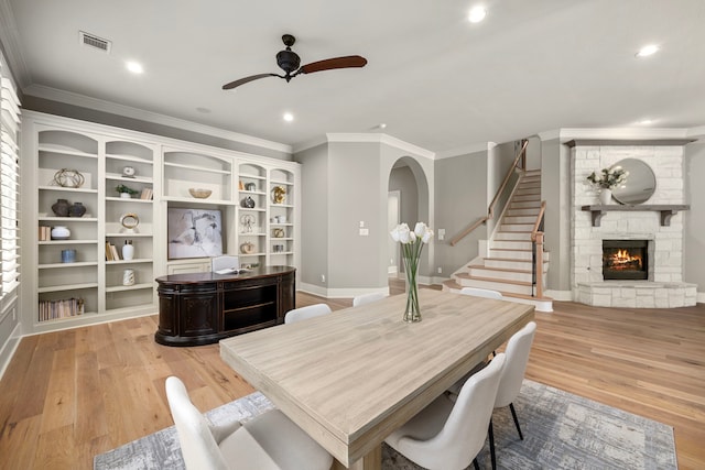 dining room featuring ceiling fan, ornamental molding, a stone fireplace, and light hardwood / wood-style floors