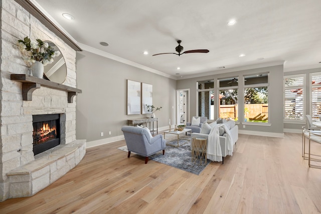 living room featuring crown molding, a stone fireplace, ceiling fan, and light hardwood / wood-style flooring